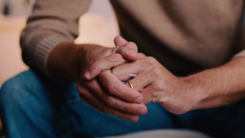 Close up of a mans hands as he touches his ring and rubs his hands together while sitting