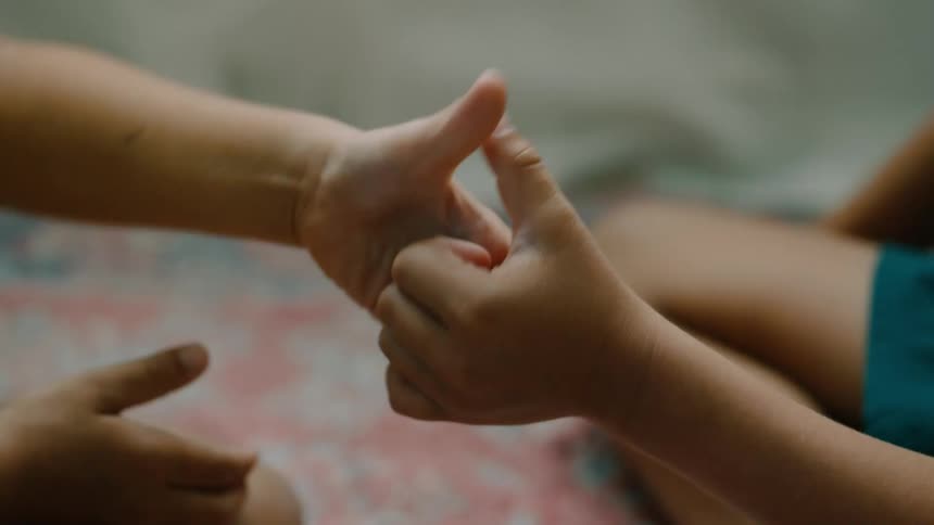 Two kids hold hands while playfully engaging in a thumb war game