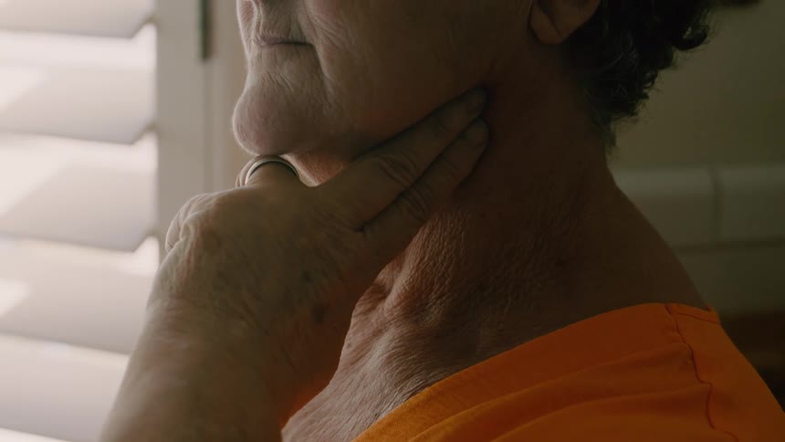 An elderly woman places two fingers on her neck to check her pulse while slowly inhaling and exhaling
