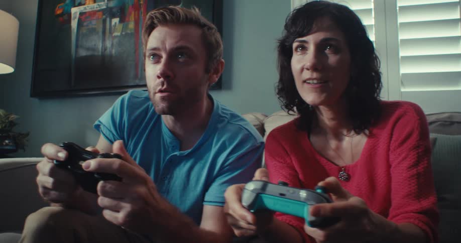 Man and woman playing video game while seated on the couch at daytime
