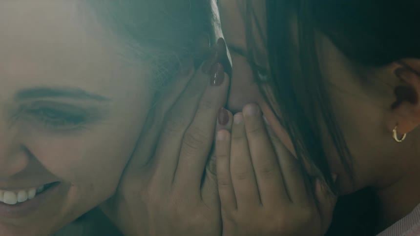 A young girl whispers a secret into her mothers ear and laughs joyfully