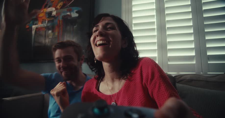 A young couple indoors excitedly celebrate winning a video game together