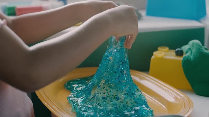 A child stretches and plays with bright blue slime on a yellow plate