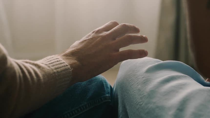A man gently reaches out to hold a womans hand but she subtly pulls away