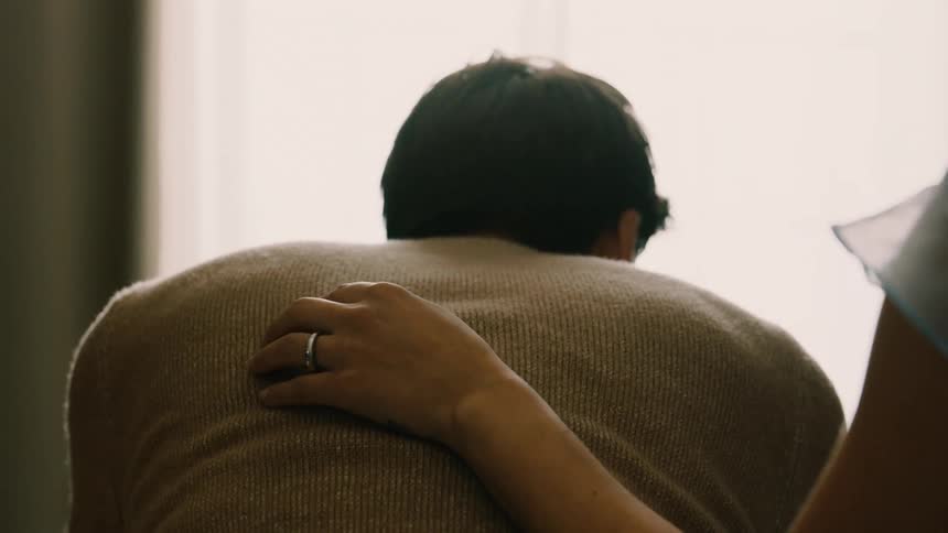 A woman gently comforts a man sitting with his head down