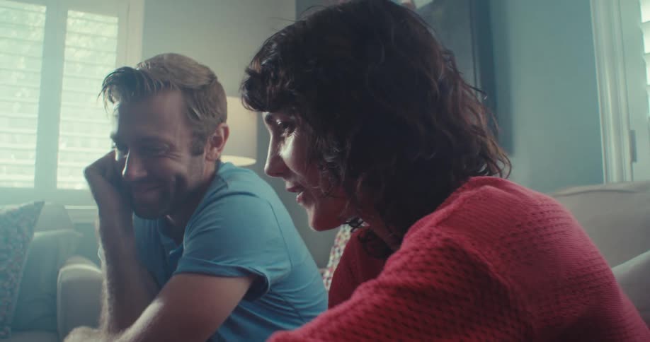 A man and a woman are sitting in a living room they are smiling and then they start looking ahead
