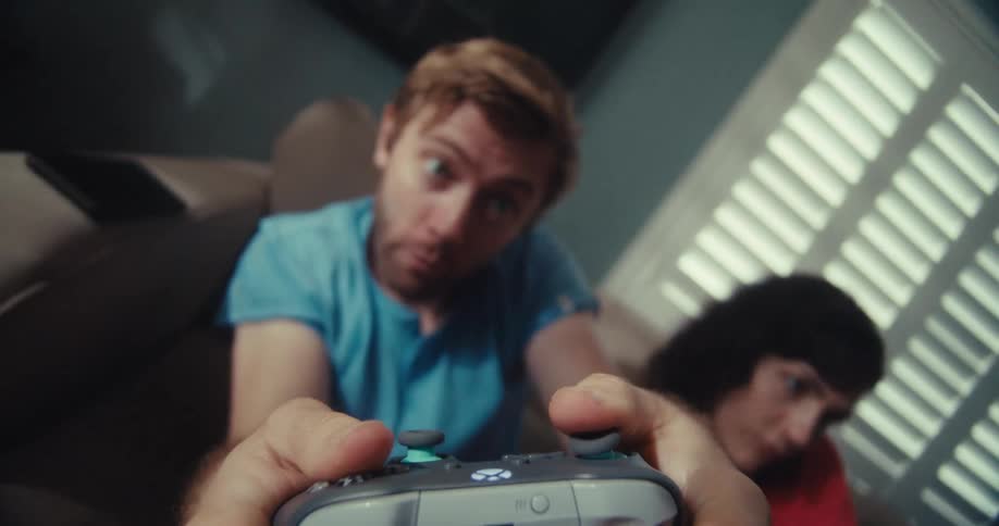 A man with wide eyes grips a video game controller while a woman beside him is also playing with a controller
