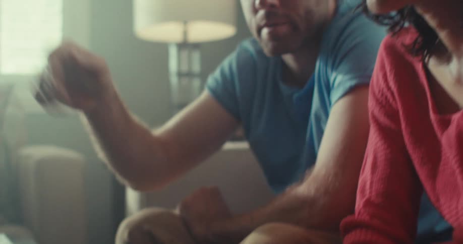 A man and a woman are sitting on a sofa and the man is using a laptop that is in front of them