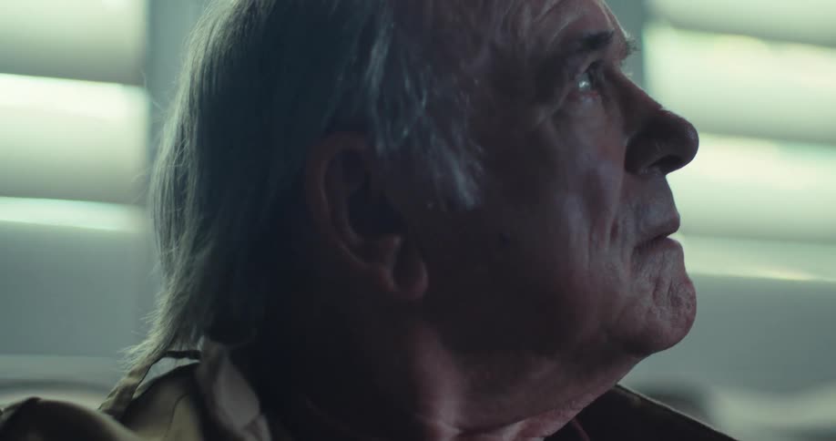 Elderly man sitting near the window and holding a pair of eyeglasses looks around