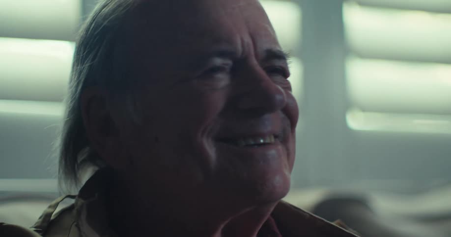 An elderly man sitting on a sofa smiling and looking ahead
