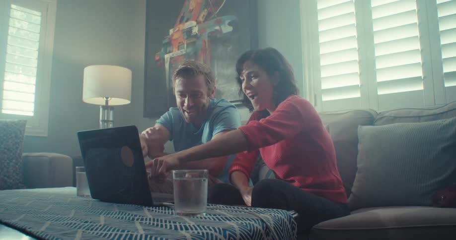 A man and woman sit on the couch whole looking at a laptop