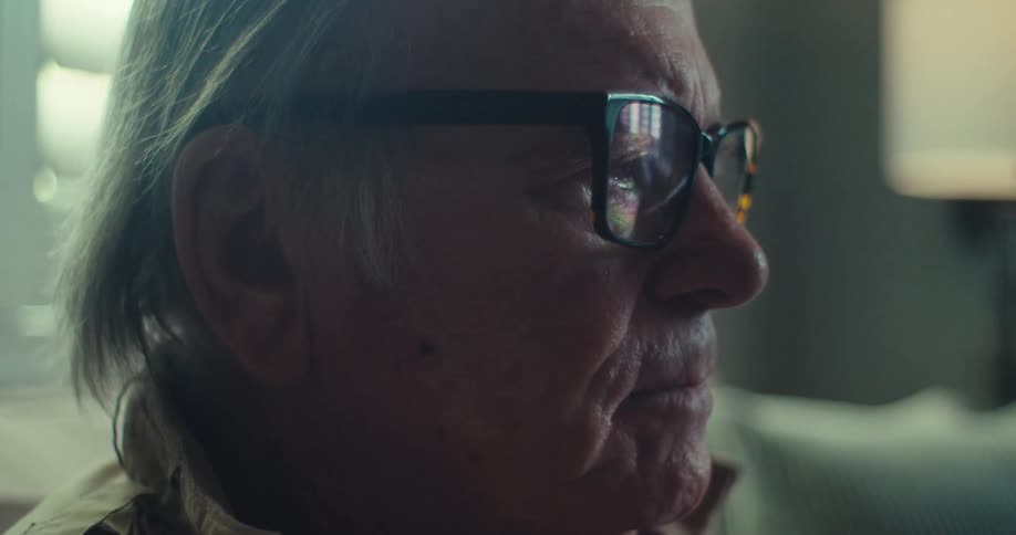 An elderly man sitting on the couch with a sad expression
