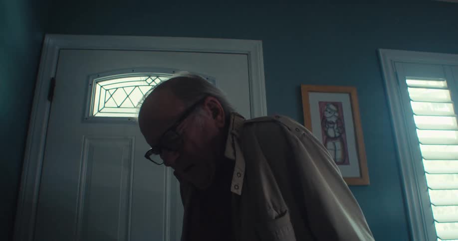 An elderly man in pain opening the door and entering the house