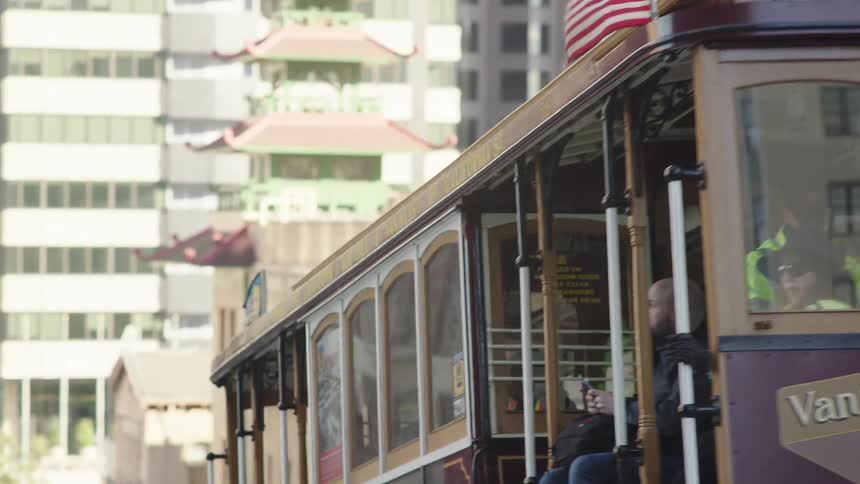 A cable car travels down the center of a city street as cars pass by on a sunny midday