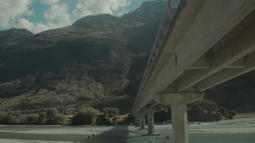 A large concrete bridge spans a river toward forested mountains beneath a partly cloudy sky