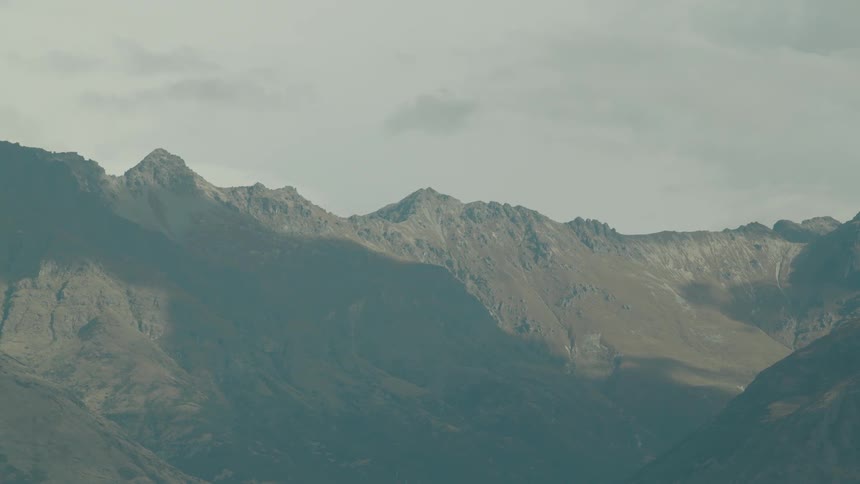 A rugged mountain range rises sharply under a cloudy sky with soft lighting