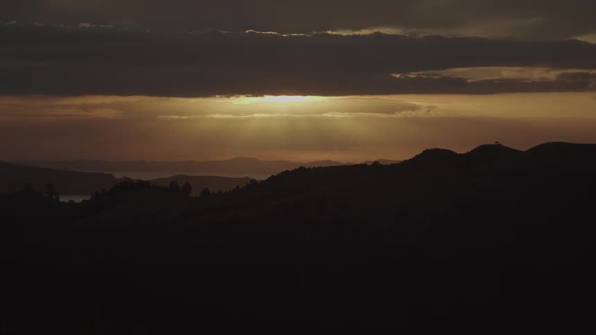 A landscape of silhouetted mointabhas and a sky with orange sunlight shining through clouds at dawn