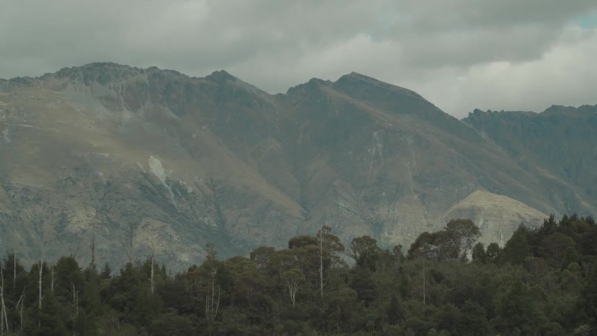 Rolling hills and mountains stretch out into the distance with some trees in the front and a cloudy sky above