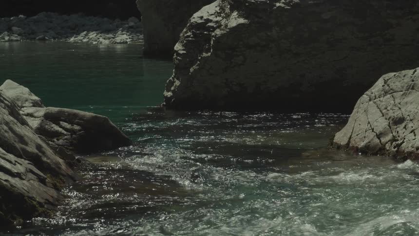 A flowing river of clear greenish water passes between large grey boulders under natural lighting