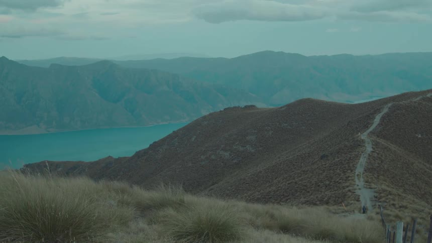 A vast mountain range stretches across the horizon partially shrouded in mist with rugged cliffs and rocky terrain in the foreground