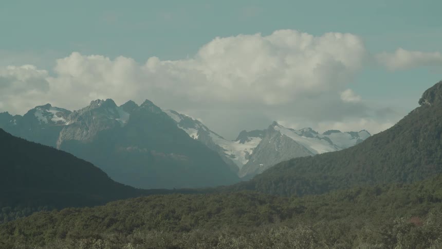 A wide view shows a mountain range with forest under a partly cloudy sky