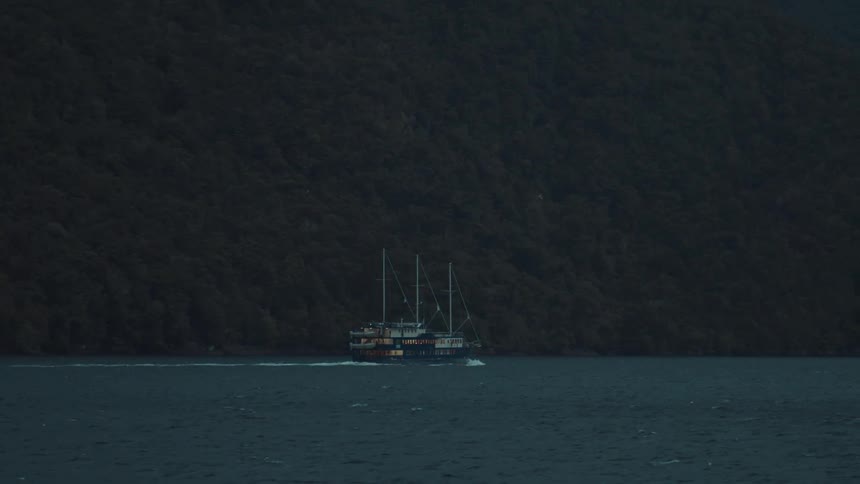 A boat sails near the shoreline in a dark moody landscape