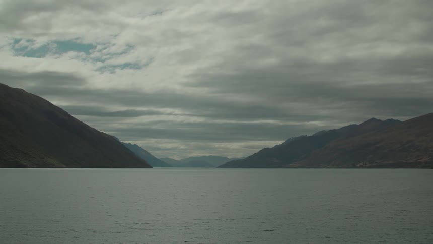 Fog covers mountainous shore under a heavily clouded sky