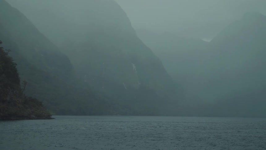 A large body of water with mountains in the background surrounded by a mist hanging over the environment