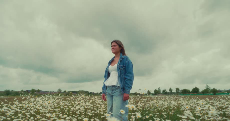 A woman wearing a blue denim jacket is standing in a field full of white flowers