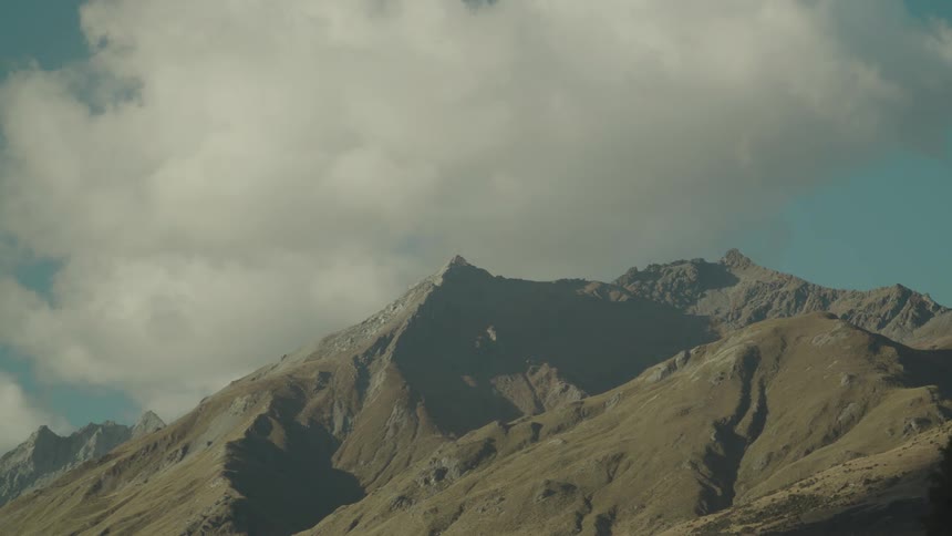 Rocky angular mountains rise towards a cloudy sky with some green slopes visible at their base