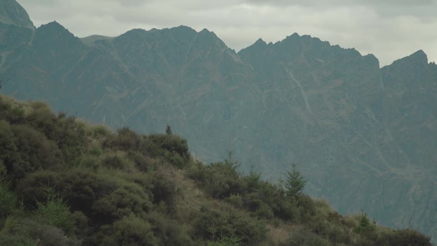 Fog obscures the jagged mountain across the valley from a grassy slope on an overcast day