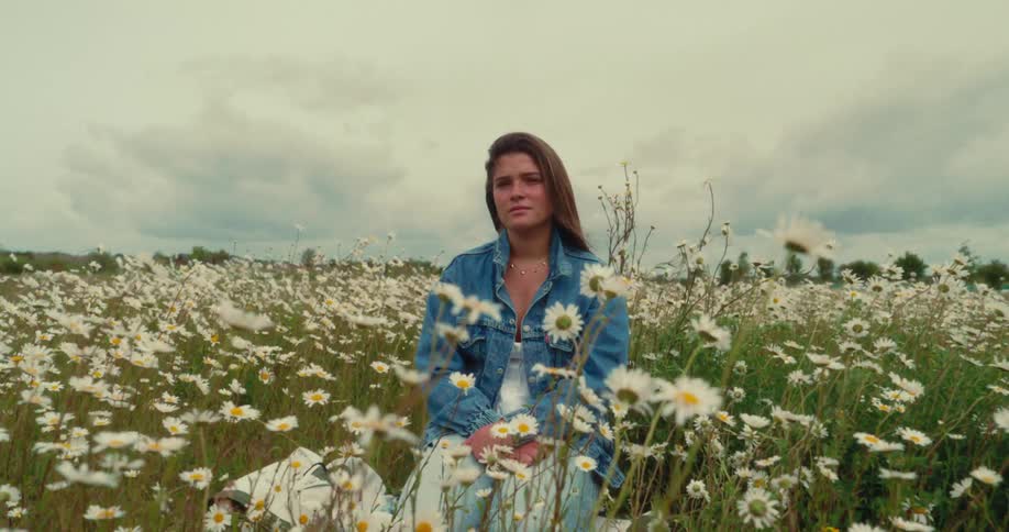 Woman sitting in a field of white daisies on a windy day