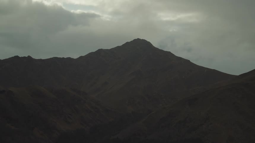 A dark silhouette of a mountain range is shown under an overcast sky