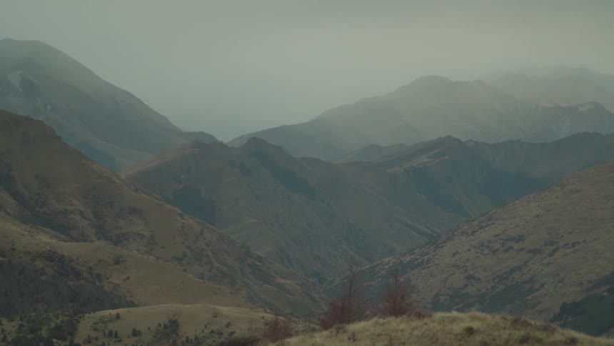 Misty mountain ridges fade into the distance beneath a grey sky