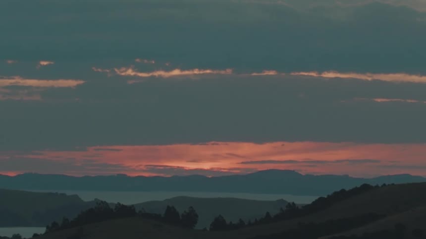 A landscape of a region with mountains and the sun in the sky shining orange between clouds