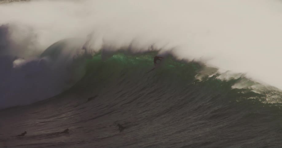 Surfers hurry to get over the top of a wave before it breaks as one surfer fails his attempt to ride it