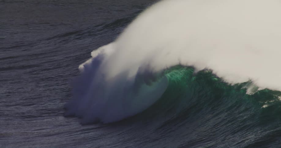 The ocean creates massive waves and splashes forming a series of white foams across the water at midday