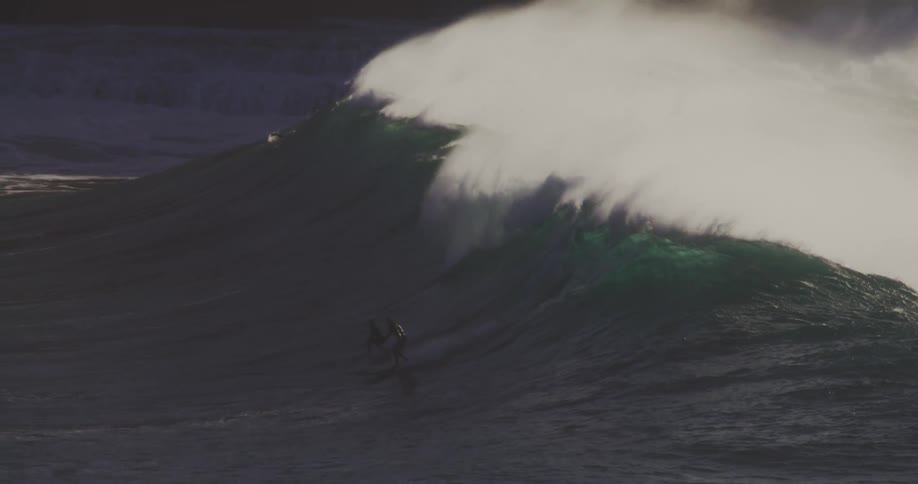 A couple surfers riding a large wave