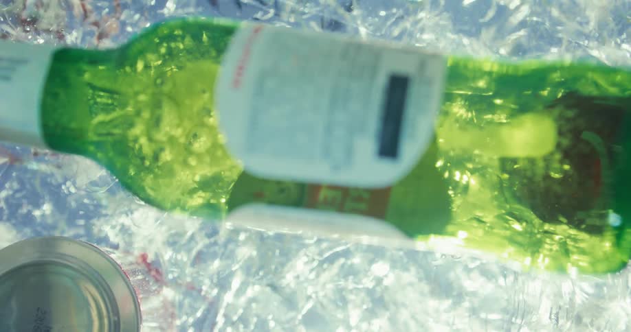 A green glass bottle is dropped into icy water