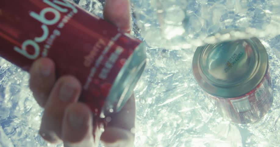 A person grabs a can of sparkling water floating in the ice