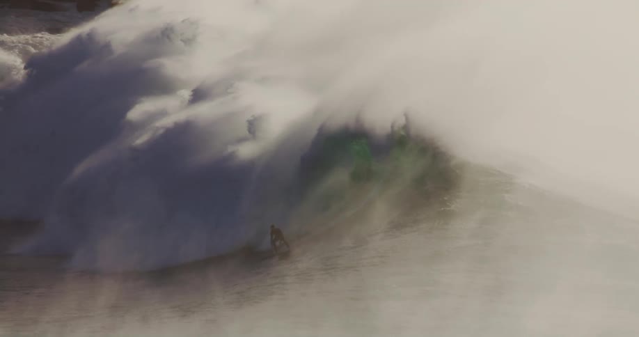 A person surfs out of a powerful ocean wave creating a dramatic splash that fills the air with foam and mist forming a foggy atmosphere over the ocean