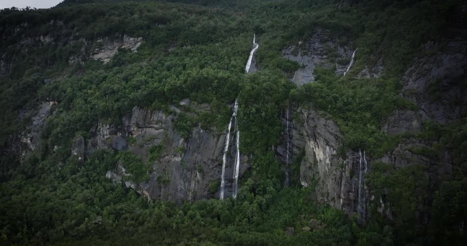 Multiple waterfalls flow down the side of the cliffs on a forested mountain
