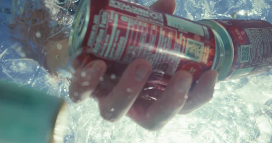 Someone reaches into icy water to grab a can of soda