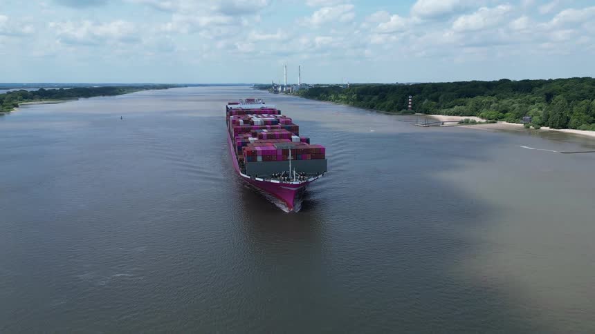 Container ship travels along a river leaving a wake on a cloudy day