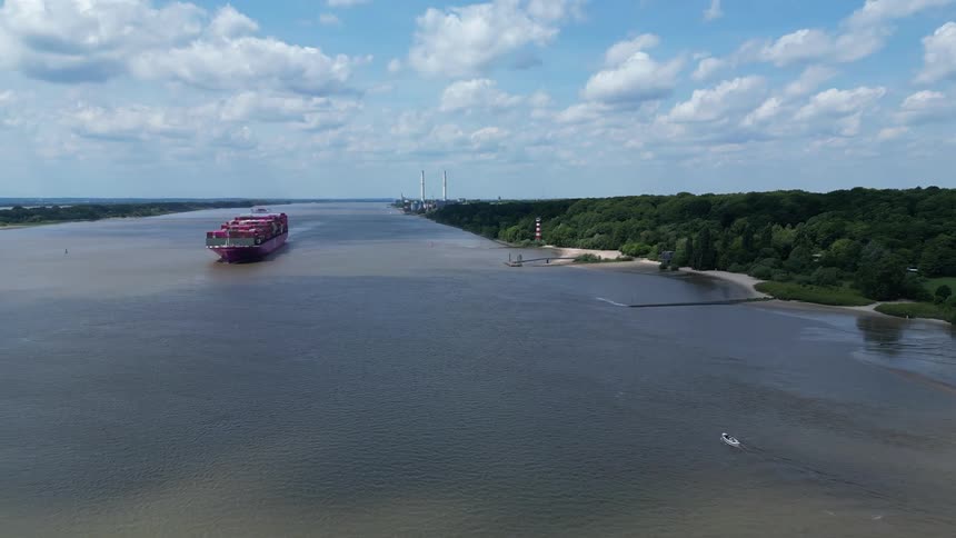 A cargo ship carrying a series of containers traveled down a river heading towards the ocean at midday