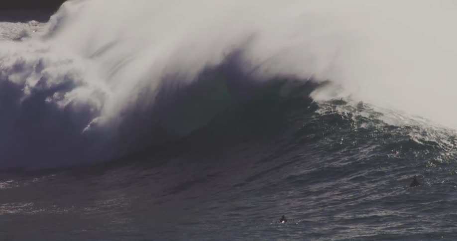 A big wave and people near the wave on surfboards watching and swimming
