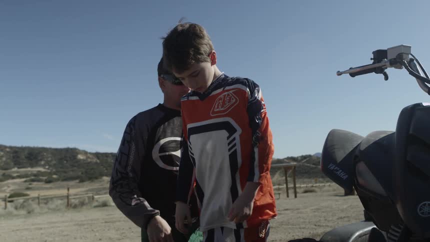 Man helps boy put on a jersey before riding