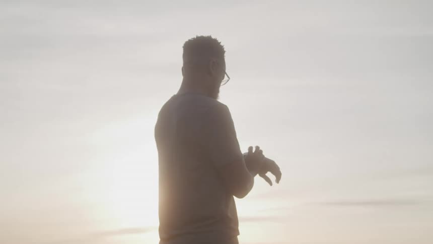 Man outdoors with reflection of sun setting a wristwatch