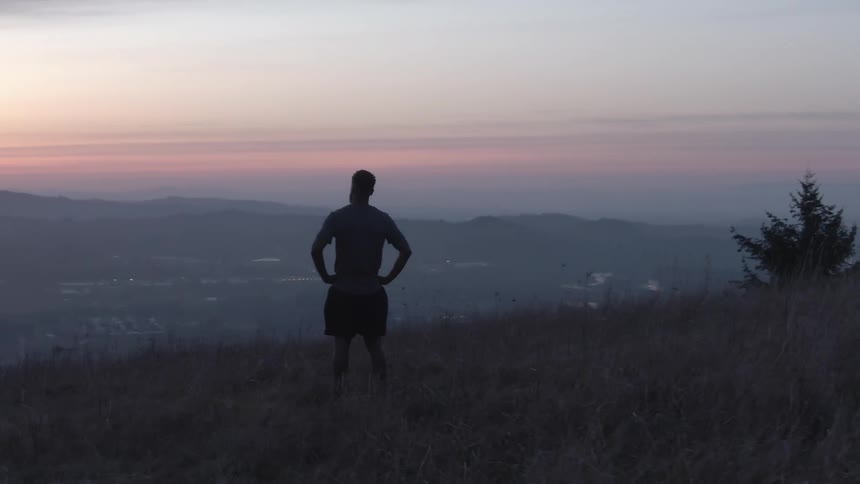 Man on a mountain with hands on hips and purple dawn sky