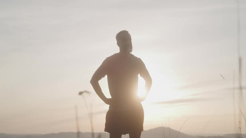 A man stands silhouetted against the setting sun
